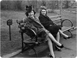 Two women pose on a park bench.
