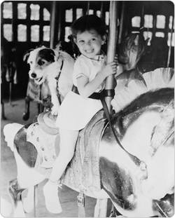 A young girl and her dog share a carousel ride.
