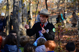 A park ranger shows feathers to a group of children around him in a park.