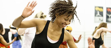 A woman leads a dance class with women dressed in African garb.