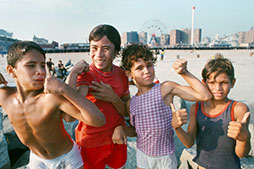 Four boys in their swim gear at Coney Island Beach pose for a photo while showing the strength of their arm muscles and showing thumbs up.