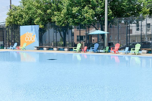 Across Fisher Pool is a yellow and blue wall with “stay cool” decals, and chairs and umbrellas at the pool side.