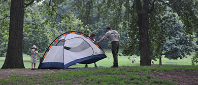 a park ranger helps a woman set up a tent in the park while a kid looks on