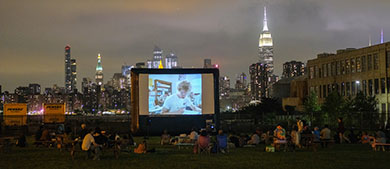 park goers watch a movie in the park while sitting on the grass or on benches