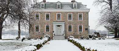 a snow covered path leads to a mansion with windows dressed up with wreaths for the holidays