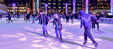 guests skate at the Bryant Park rink at night when the rink is lit up purple