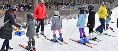 an instructor teaches kids how to ski on a snow covered landscape in the park