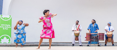 Dancers perform to the beat of drums played on stage in a park. A sign near the stage reads NYC Parks Arts, Culture & Fun.