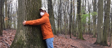 an educator wearing a mask hugs a tree in the forest