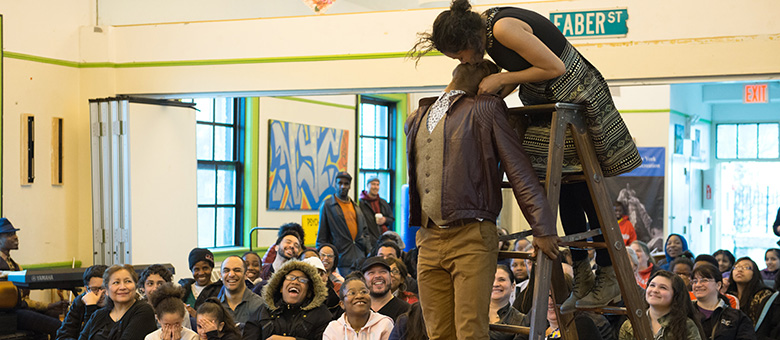 The crowd in the rec center looks on in awe as an actress playing Juliet leans in from the steps on a ladder to give Romeo a kiss upside down.