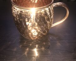 A photo of a gleaming brass coffee mug with lighting effects on the rim.