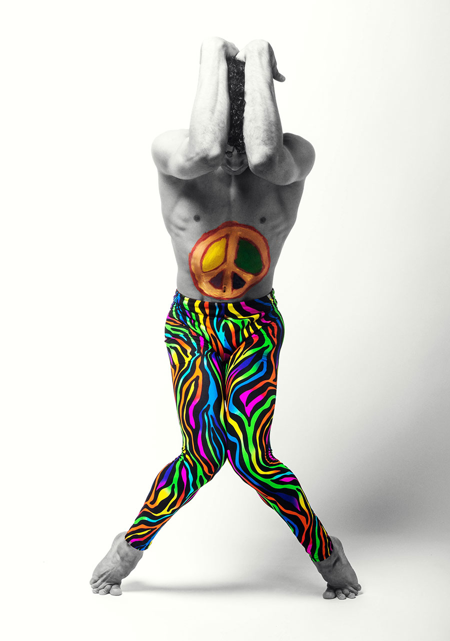 Image of a person wearing zebra print pants in pride colors holding their arms in a cowering position over their head. A peace sign in orange, yellow, and black is painted on the tummy.
