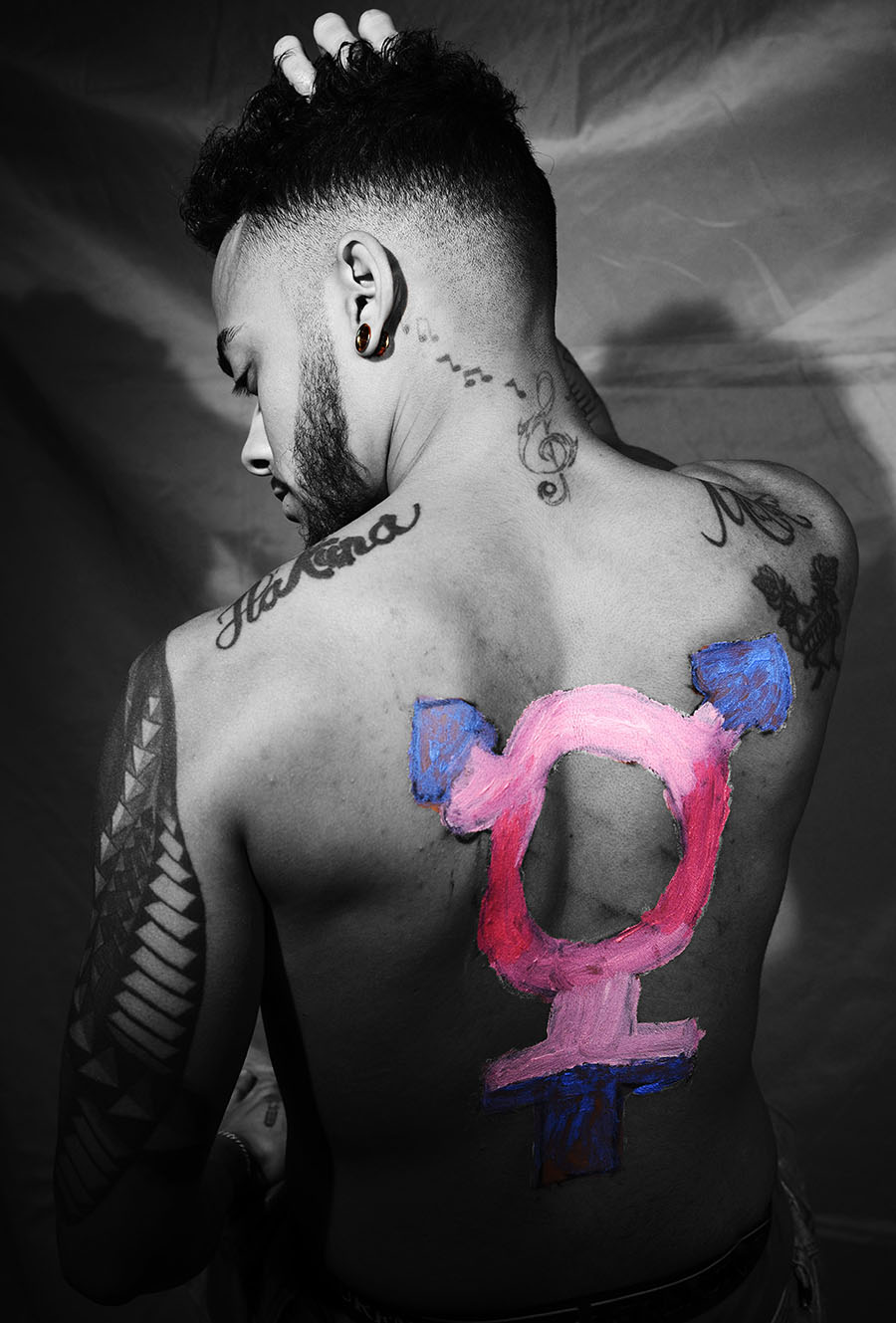 Black an white image of a pink and blue equality sign painted on the back of someone with tattoos