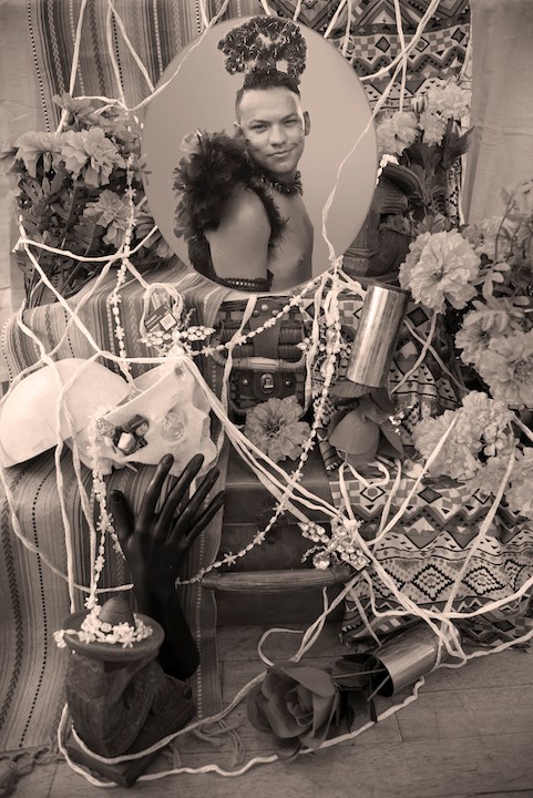 Circular framed image of a person dressed up on an altar with flowers, strings, jewelry and other keepsakes
