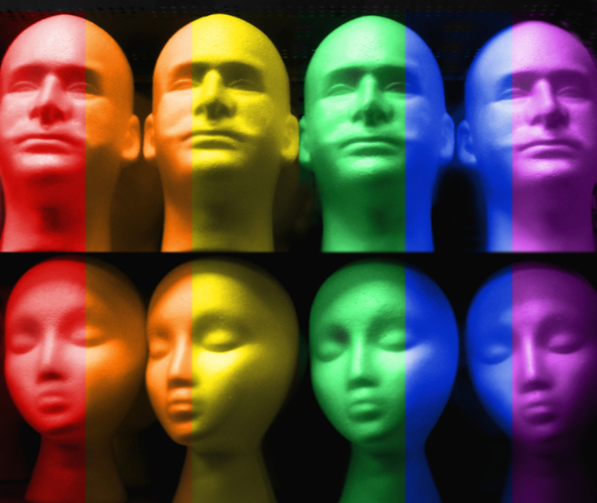 Molds of heads of humans are arranged in two rows, 4 heads per row. They were graphically splashed with the pride colors