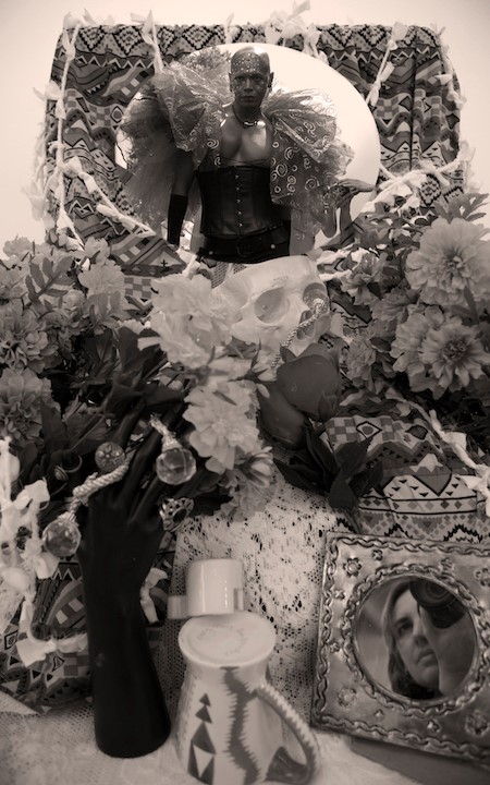 Image of a person dressed up on an altar surrounded by flowers, skulls, and jewelry