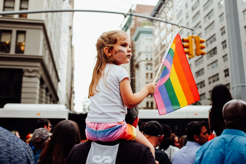A child on the shoulders of her dad waves her pride flag during the pride parade