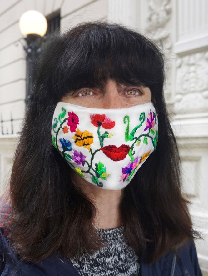 The artist wears a mask that features flowers, plants, and lips embroidered on it