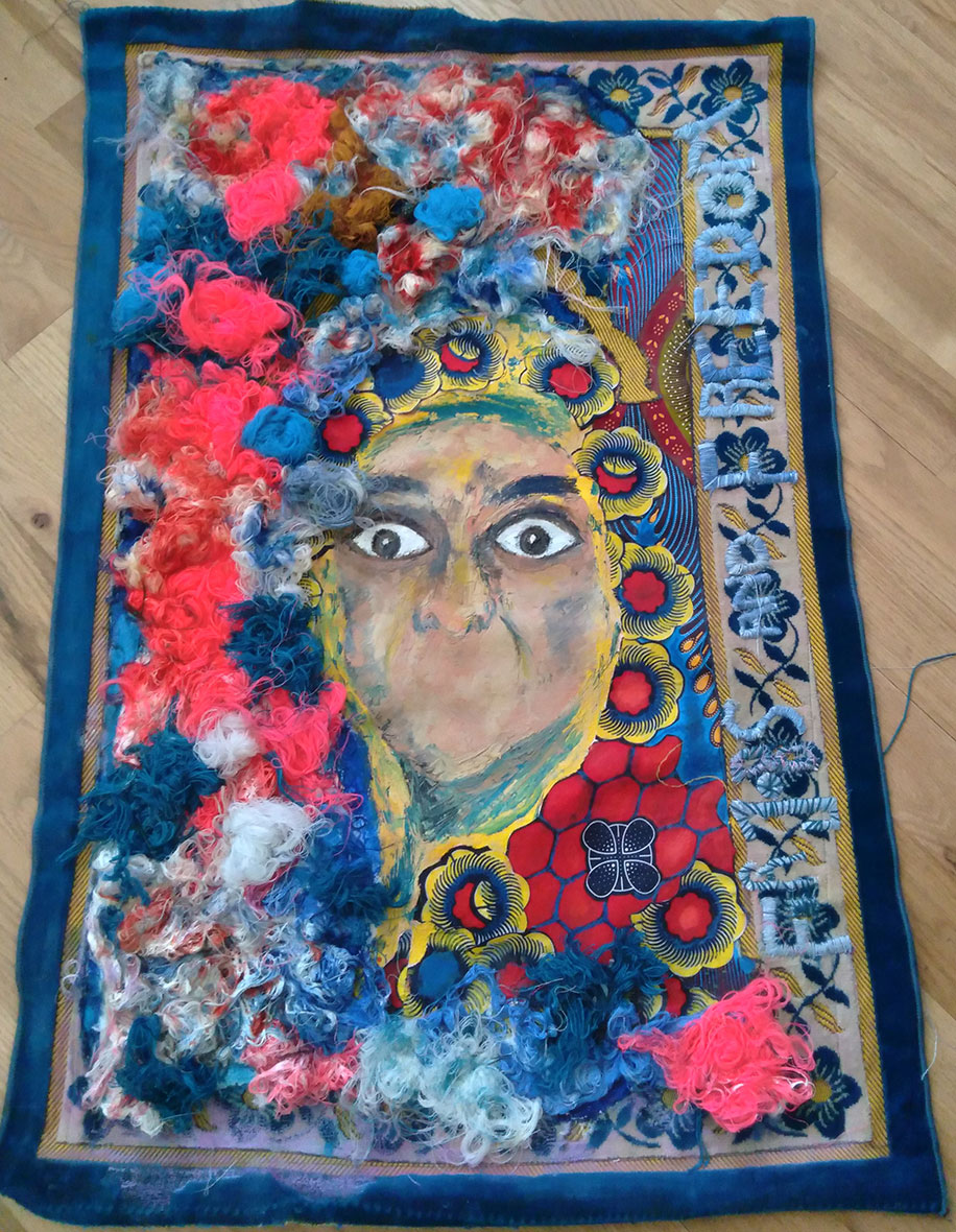 A mouthless person with eyes wide is surrounded by embroidery patches in pink, blue, and red; words embroidered down the side of the vanvas reads for jobs and freedom