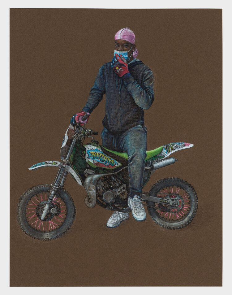 A Black biker wearing a pink dur rag holds a blue mask to his face while standing over his bike