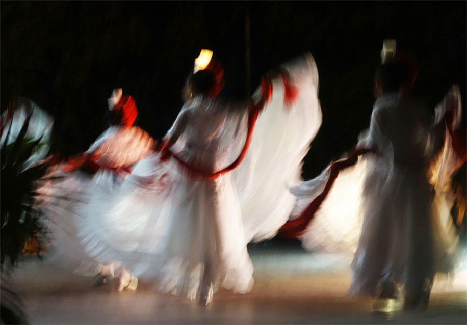 Women dressed in white long dresses dance into the night at a performance