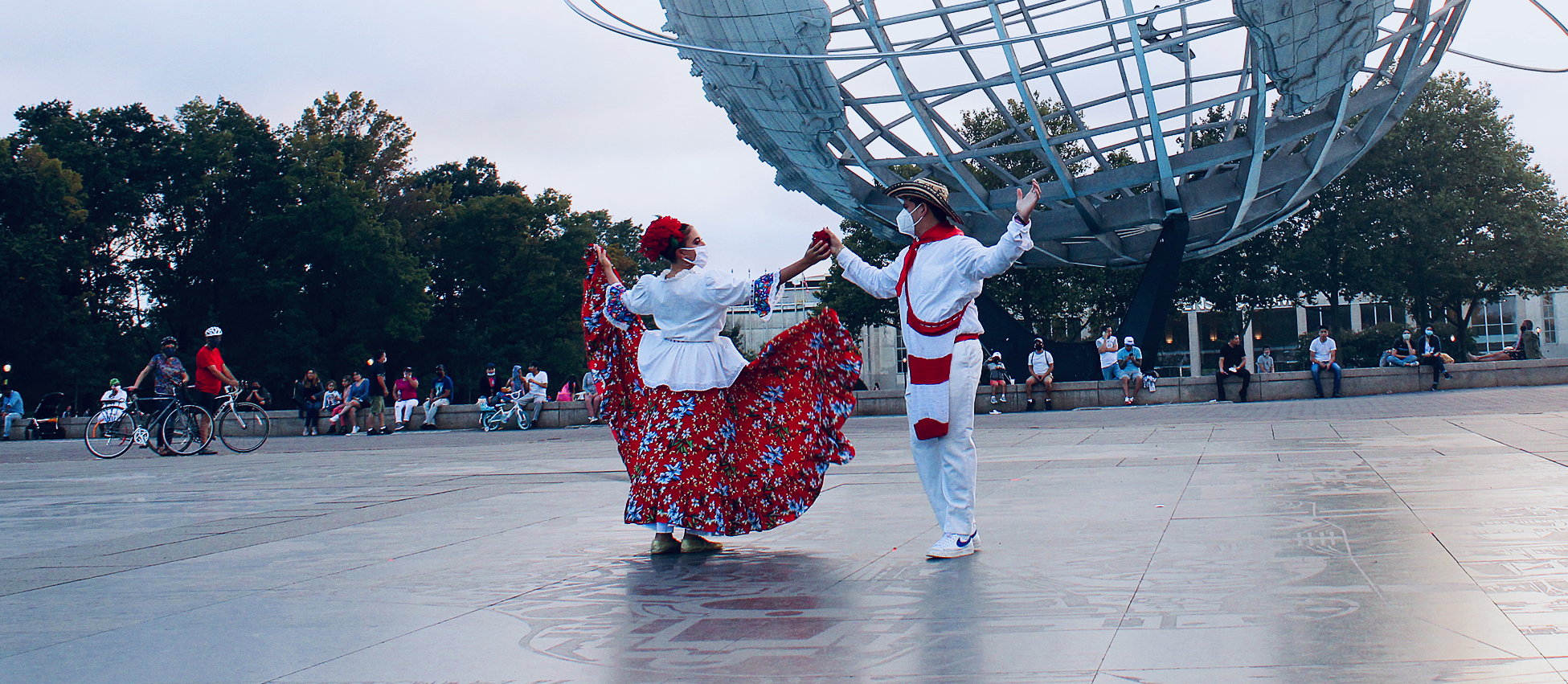 Dancers in traditional Mexican attire performs for an audience in the park in front of the Unisphere which is a giant steel globe