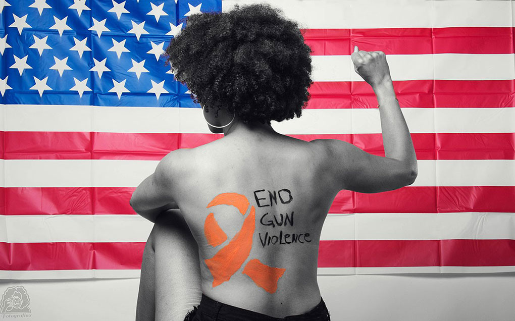 A woman holding up a fist faces the American flag. On her back are the words End Gun Violence