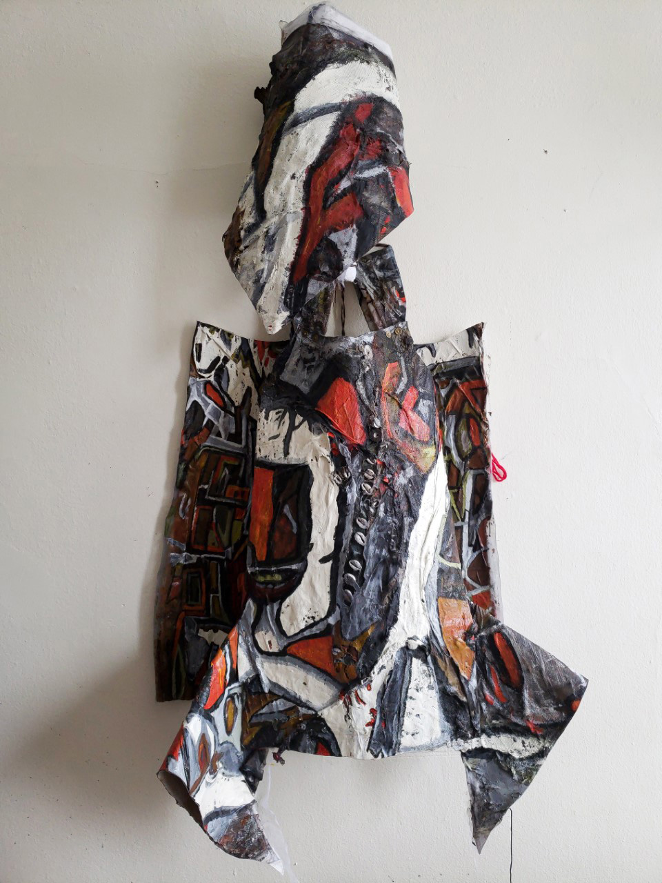 a layering of fabric form a figure that is painted on in red, orange, gray, and black colors