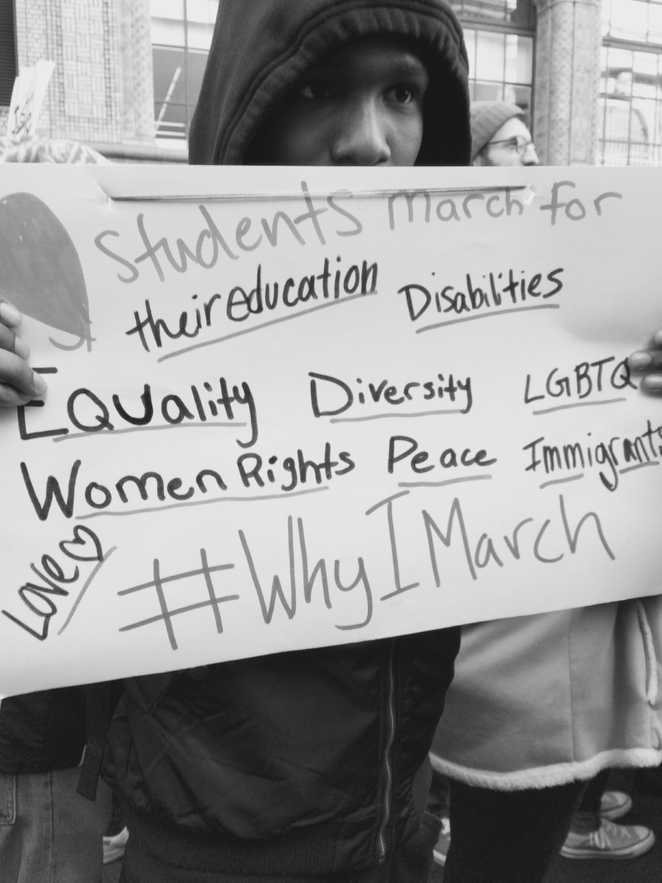 a protestor holds up a sign that reads Students march for their education, disabilities, equality, diversity, lgbtq, women's rights, peace, immigrants, love, hashtag why we march