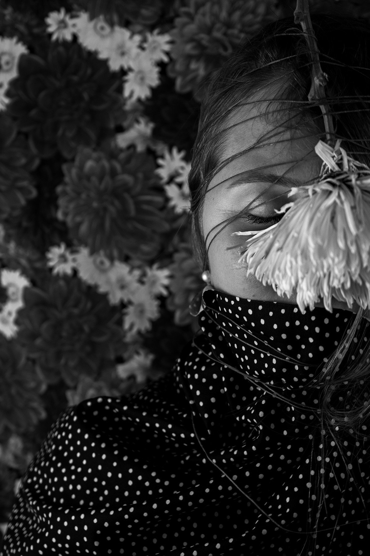 black and white photo of a woman with a white flower hanging from her forehead, her eyes closed, the flower covers most of her face