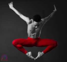 A dancer wearing red pants leaps into the air