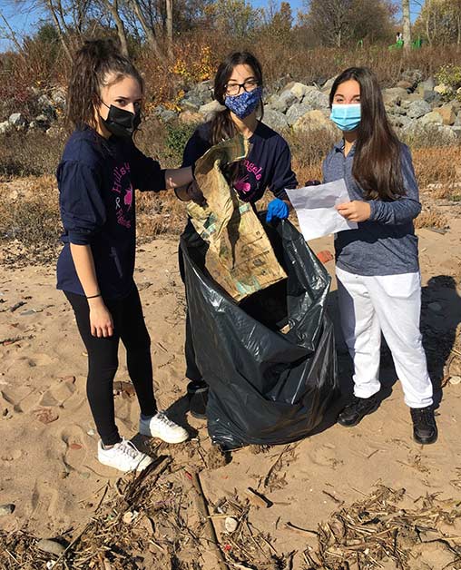 Students place cardboard trash into a bag while on a volunteer cleanup at a City beach.