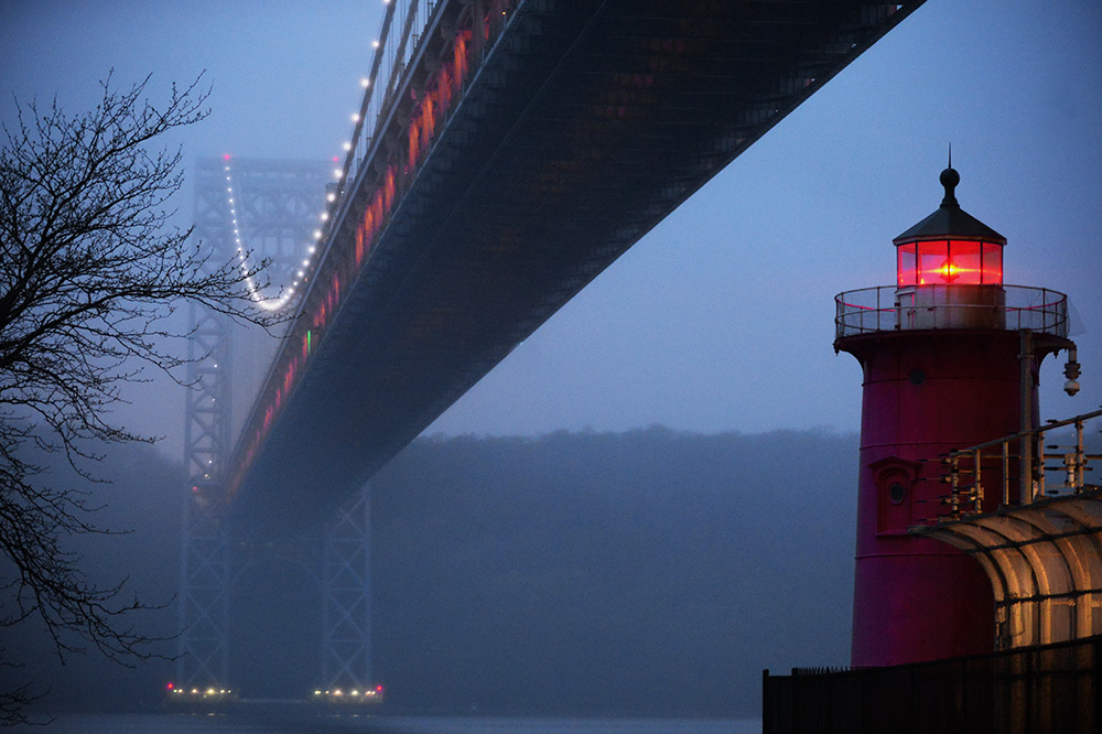 a red lighthouse under a bridge is surrounded by fog at night