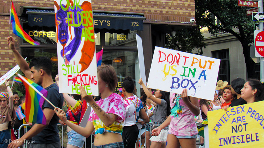 Parade participants hold up signs that read: Our elders are still f-ing here, don't put us in a box, intersex people are not invisible
