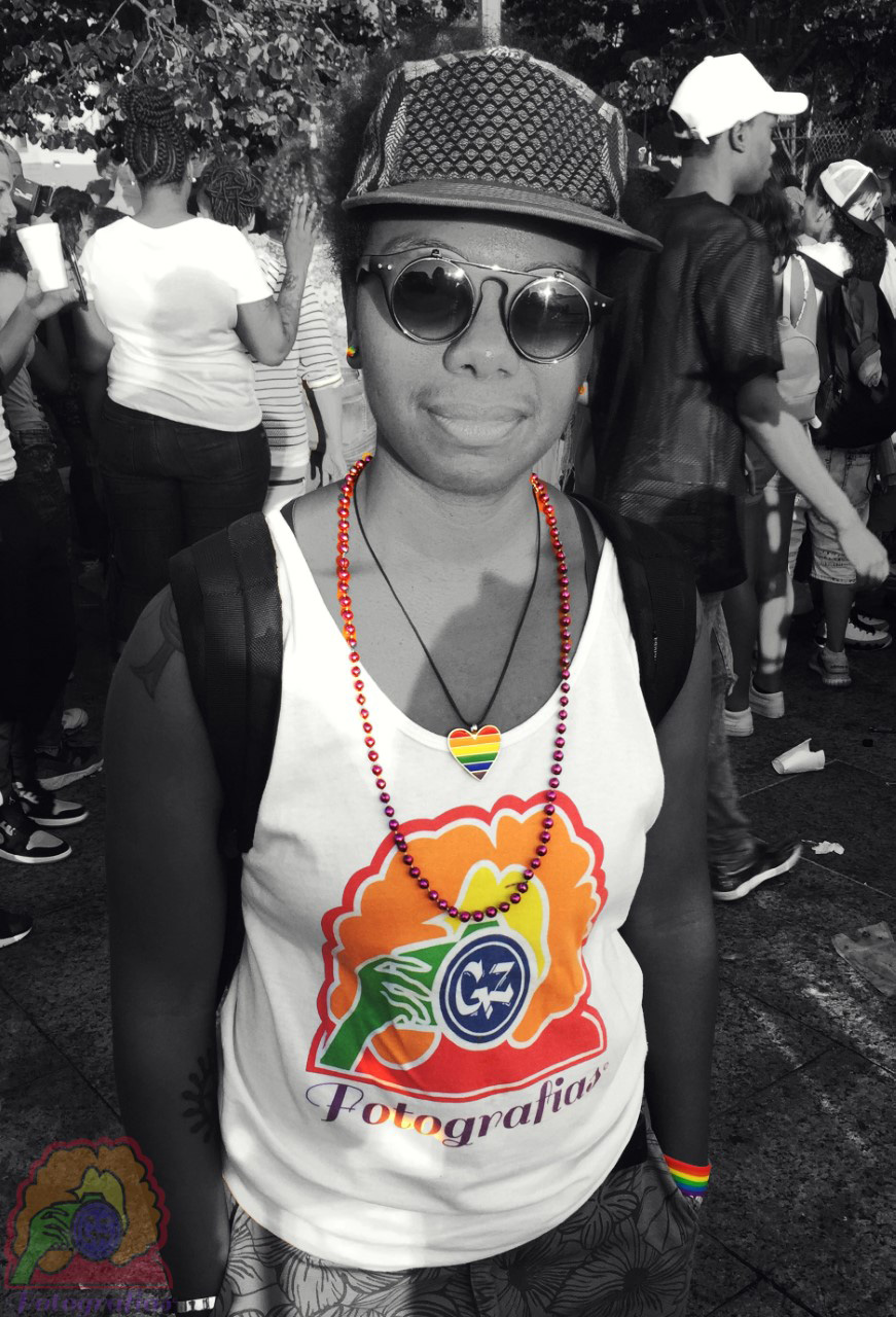 black and white portrait of the artist in a crowd, and wearing (in color) a Pride necklace, beads, and a brand shirt