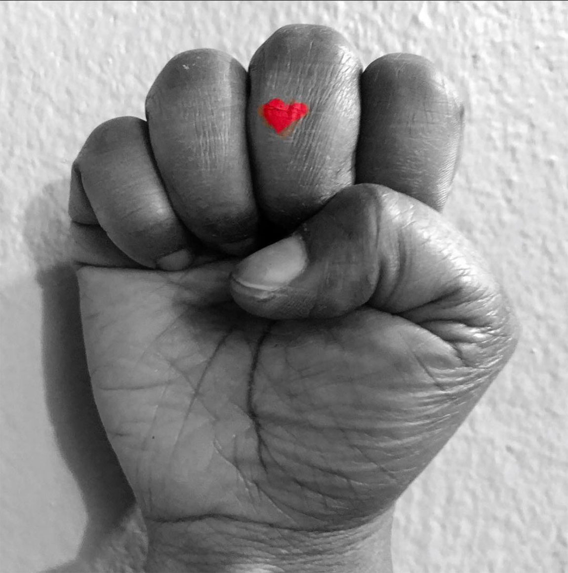 black and white photo of a fist with a red hard painted on the middle finger