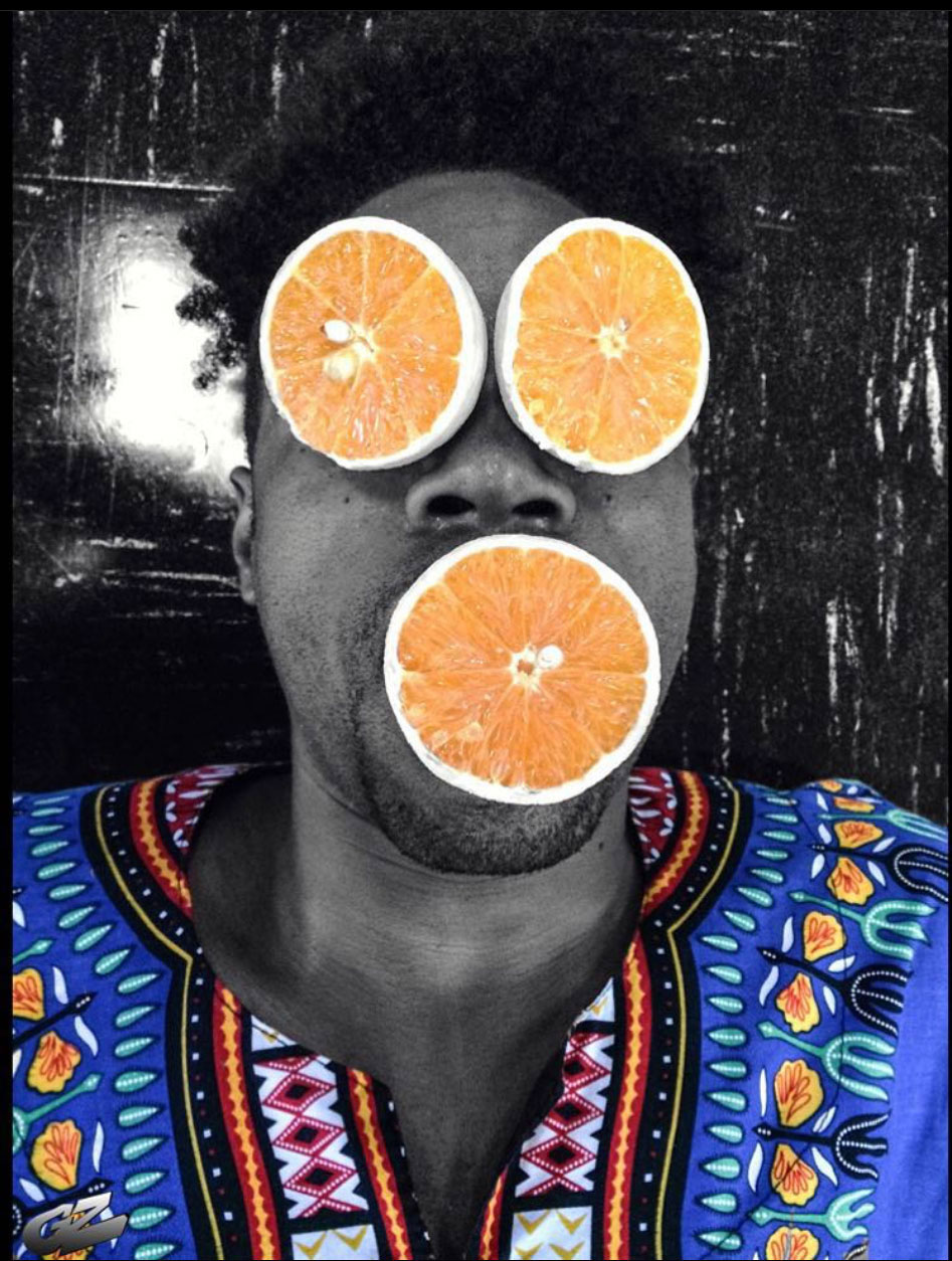 photo of an individual with orange slices for eyes and a month, the individual is wearing a dashiki with highlights of orange colors as well as blue, green, white, black, and red