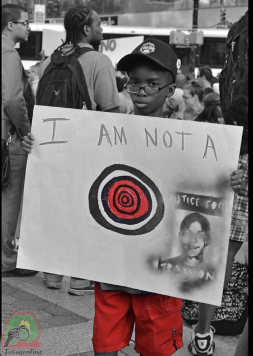 black and white photo of a child holding up a sign that reads: I am not a target; justice for Trayvon. The target is highlighted in color