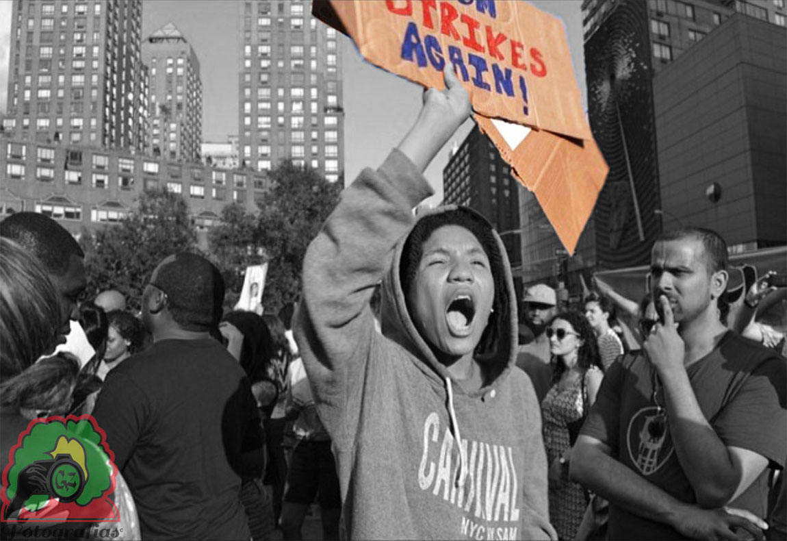 black and white image of a protest in Union Square, in color is one of the signs held up that shows the word Strikes Again