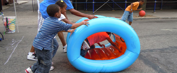 Kids pushing an inflatable wheel with another kid inside