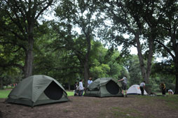 The Urban Park Rangers and guests set up camping tents in an open space in the park.